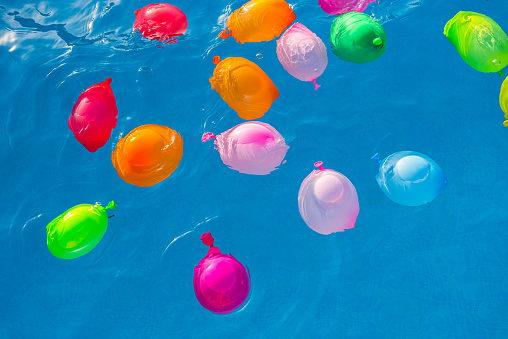 Group of many colorful plastic water balloons floating in the water of a pool to entertain their children on summer vacations.
