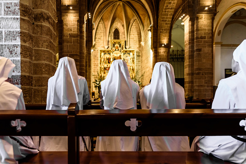 Valencia, Spain - September 25, 2019: Group of Christian nuns with white robes praying in a church.