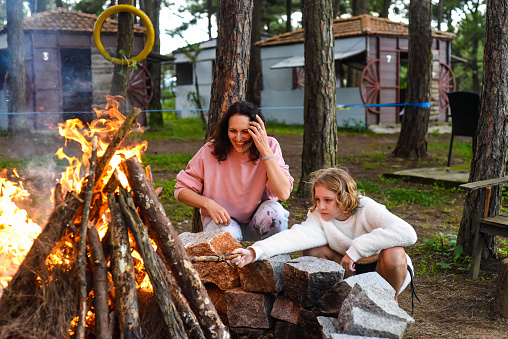 Mother with her little daughter spending time together, kindle a fire and throw sticks