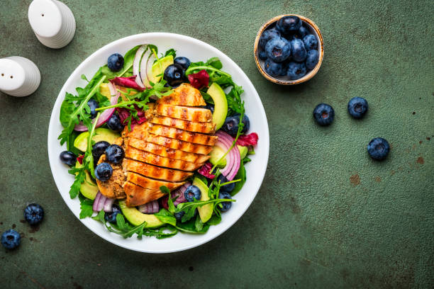 istock Delicious salad with blueberries, grilled chicken, avocado, red onion, walnuts, arugula and mixed herbs, green table background, top view 1711236473