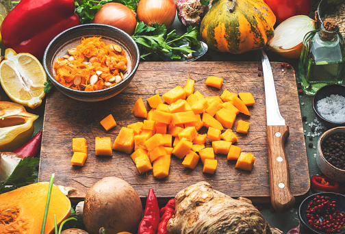 Food background. Diced raw peeled pumpkin and vegetable knife on rustic wooden cutting board. Vegetables, mushrooms, roots, spices - ingredients for vegan cooking. Healthy eating, diet, comfort slow food concept. Top view