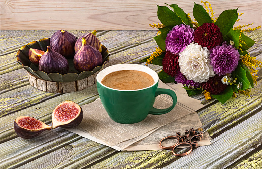 Fresh ripe figs on vintage plate, green cup of coffee, bouquet of burgundy dahlias, vintage scissors and purple shawl as decor. Autumn still life