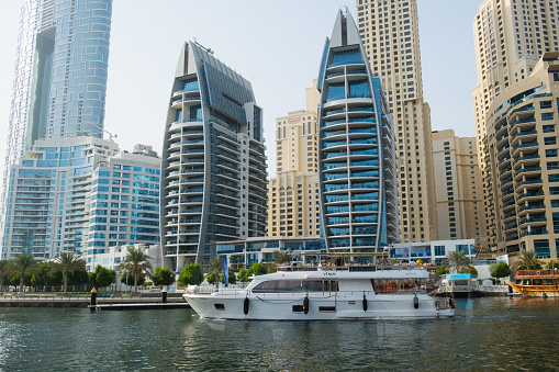 View of the skyscrapers of Dubai Marina from the water. White yacht in the city bay. Modern city of the United Arab Emirates. Dubai, UAE - 09.23.2023