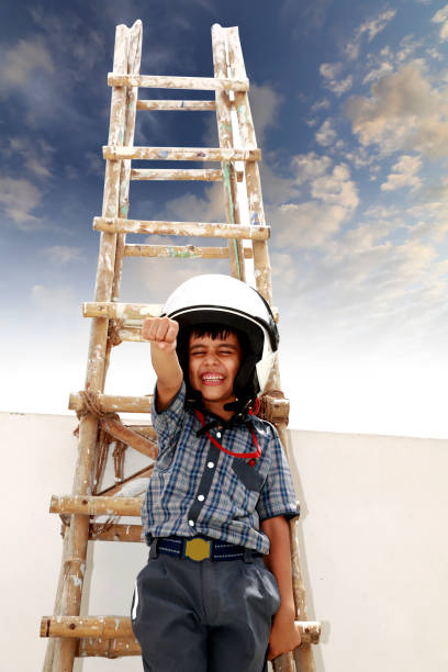 Cheerful elementary age child of Indian ethnicity posing flying in the sky near ladder of success wearing school uniform.