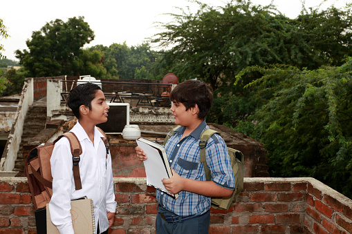 Two primary or high school student wearing school uniform discussing something face to face after school vacation at home also carrying school bag.