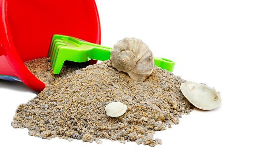 Toy bucket and rake with sand and shells on a white background