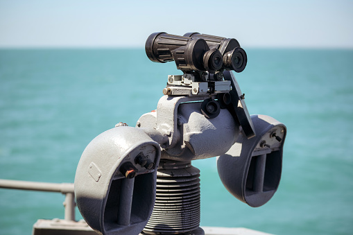 A landscape image of a viewing telescope on the harbour wall in the quaint harbour of the picturesque fishing village of Mousehole in Cornwall, UK which is a popular tourist destination on a beautiful summer day.
