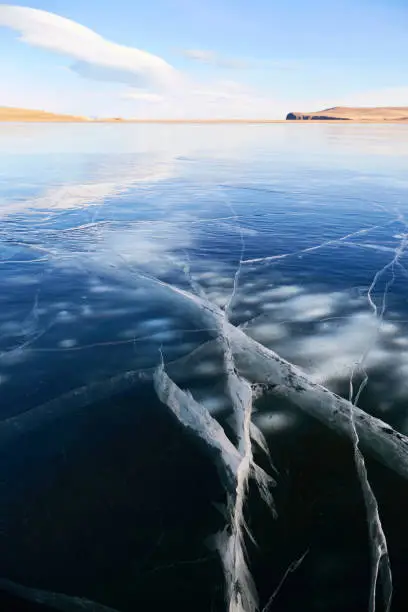 Frozen Lake Baikal on a sunny winter day. Transparent smooth ice with cracks. Natural background. Vertical orientation.