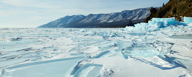 Winter landscape, panorama. Frozen Lake Baikal, picturesque mountains, huge blocks of transparent blue ice, hummocks.