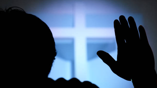 istock Silhouette Hand raising, blurred christian cross background 1711335323