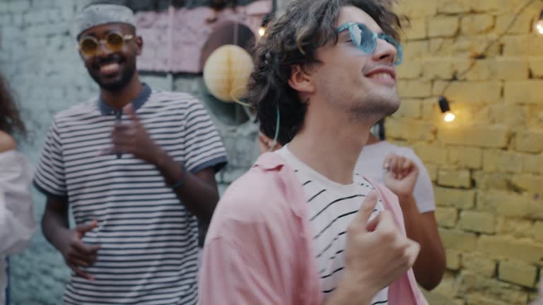 Portrait of carefree guy dancing celebrating holiday with friends enjoying music in terrace cafe