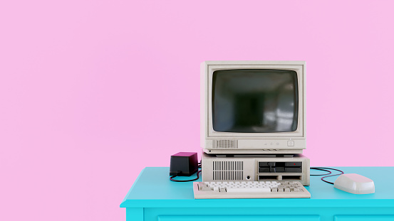 Old computer from the 1980s stands on a desk. It has a small screen, keyboard and a computer mouse. The colors a typical of the 1980s: Pink and cyan mixed. Room for copy space.