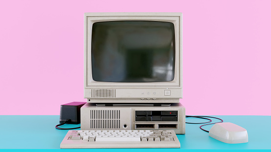 Old computer from the 1980s stands on a desk. It has a small screen, keyboard and a computer mouse. The colors a typical of the 1980s: Pink and cyan mixed. Room for copy space.