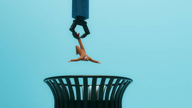 Big robotic arm has grapped a man in a business suit and gets ready to dispose of him and throw him in the trash. Concept of AI and robots taking over making human obsolete.