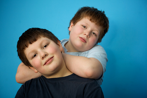 siblings: cute overweight boys in front of blue wall, looking to camera