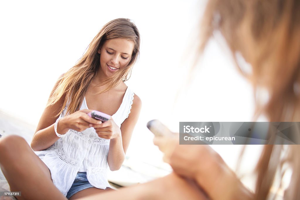 Duas meninas feliz adolescente mensagens de texto, na praia - Foto de stock de 18-19 Anos royalty-free