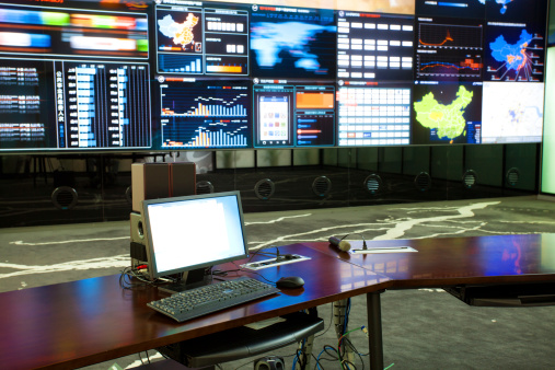 Trader holding cup of coffee and text messaging on smart phone while sitting in front of stock market reports on computer screens at workplace