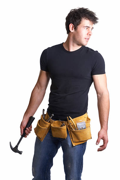 Handsome repairman wearing tool belt with hammer in hand Handsome repairman wearing tool belt with  hammer in hand, looking away, against white background tool belt stock pictures, royalty-free photos & images