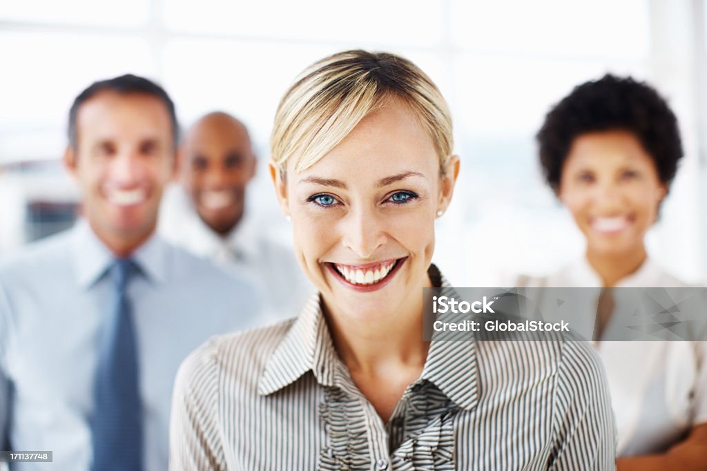 Empresaria sonriente con colegas en el fondo - Foto de stock de Adulto libre de derechos