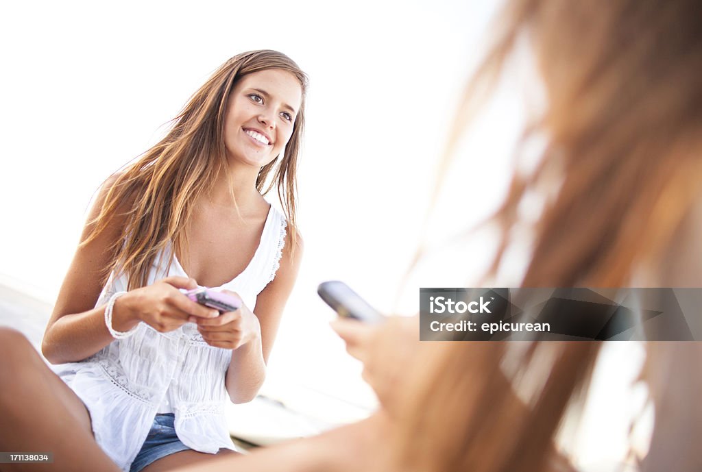 Due ragazze adolescenti felici i messaggi di testo sulla spiaggia - Foto stock royalty-free di 18-19 anni