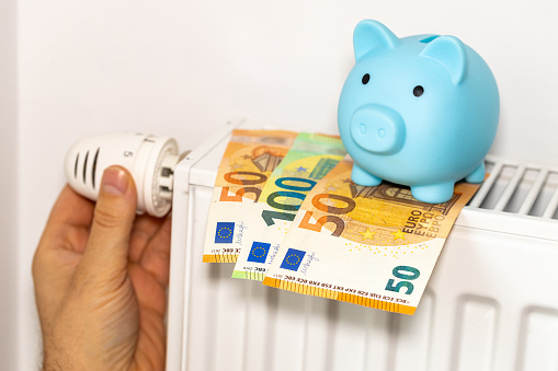 costs of heating apartments in winter in the European Union, energy and economic concept, hand unscrewing the radiator, piggy bank and euro money