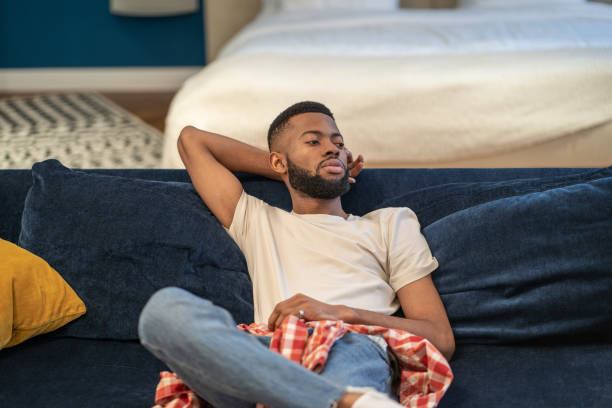 istock Thoughtful dreaming african american guy sits on sofa rests in studio apartment. 1711406533