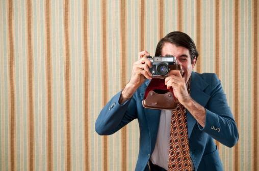 Nerdy tourist in a blue retro suit taking a picture with a  vintage camera. The wall has a striped wallpaper.Take a look at my LIGHTBOXES of other related images.