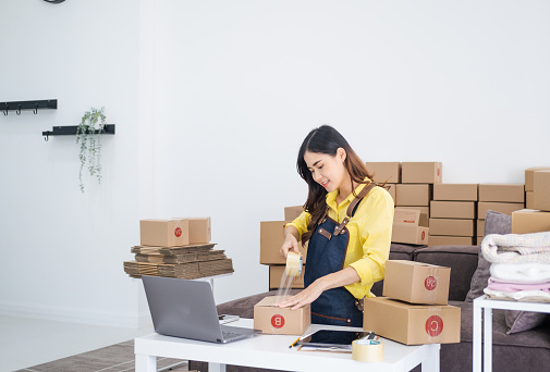 Small business owner packing in the cardbox at home office. Woman preparing a parcel for delivery at online selling business office. Entrepreneurs Arranging Goods With Parcel Boxes Startup Ideas.
