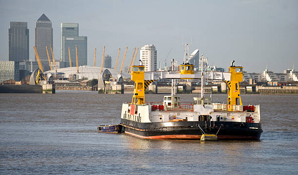 A view of the Woolwich Ferry with the towers of Canary wharf and the millenium dome in the background.