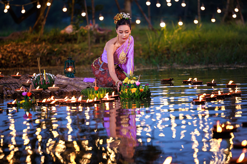 Loi Krathong Festival, Thai woman holding a krathong sitting on a raft by the river, Asian women in traditional Thai costumes bring krathongs to float on Loi Krathong Day, traditions and culture of Thailand,