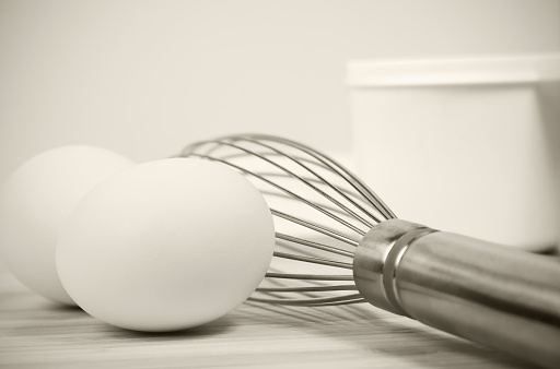 Eggs with a stainless steel wire whisk on a wooden surface with a measuring cup in the background.