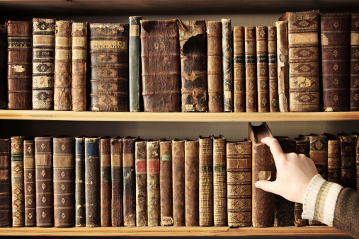 Male hand picking a book from a row of antique books. Photo was taken at avaible light, and it is slightly toned to enhance the old condition of the books.