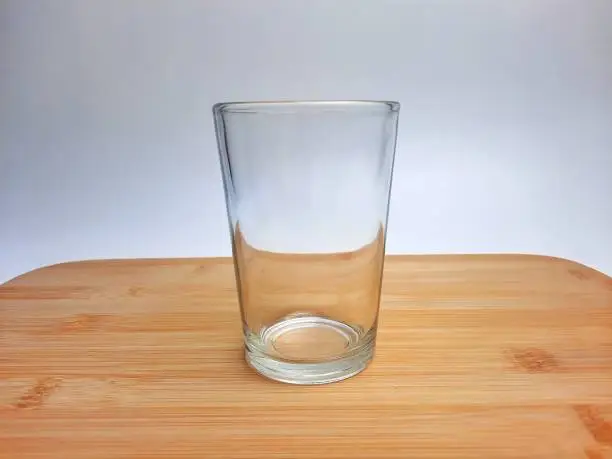Photo of Empty drinking glass cup with copy space. Glass cup with wooden coaster