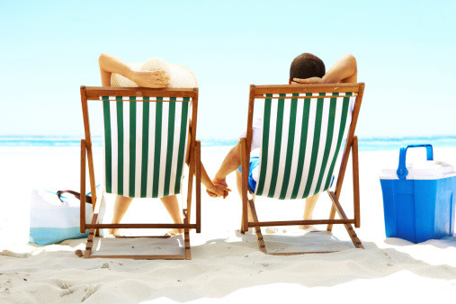 Couple sitting relaxing in deck chairs while on the beach and holding hands