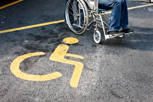 This disabled person in a wheelchair is parked right next to the sign for disabled parking. Shot with Canon EOS 1Ds Mark III.