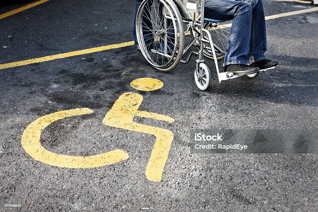 Pessoas em cadeira de rodas ao lado de uma placa de estacionamento para visitantes com necessidades especiais - Foto de stock de Estacionamento de carros royalty-free