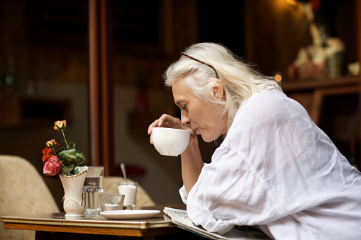 mature woman sits in a cafe, drinks a hot drink and reads the newspaper