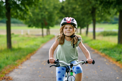 Little preschool girl riding bike. Kid on bicycle outdoors. Happy child enjoying bike ride on her way to school on warm summer day. Preschooler learning to balance on bicycle in safe helmet
