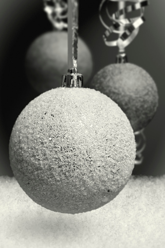 Christmas decoration: three Cristmas balls on silver ribbons. Black & White old-stylized photograph. The depth of field is ultra shallow. Light yellow tone. Very light film grain on background. Real snow. Color space Adobe RGB (1998).