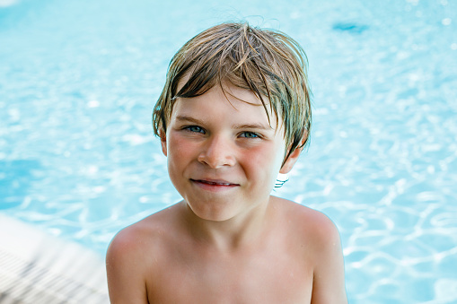Portrait of happy little kid boy resting near the pool and having fun on family vacations in a hotel resort. Healthy child playing in water, swimming and splashing