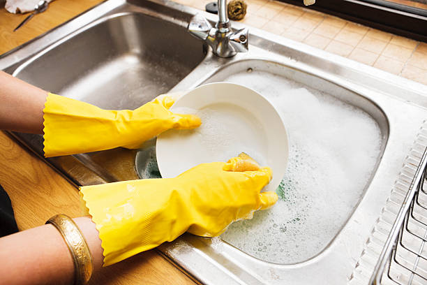 View over shoulder of young woman doing the dishes Looking over the shoulder of a young woman in rubber gloves doing the dishes. Shot with Canon EOS 1Ds Mark III. wash dishes stock pictures, royalty-free photos & images