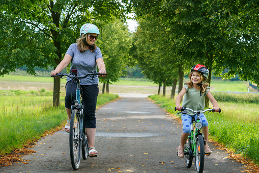 Happy family is riding bikes outdoors and smiling. Mother and daughter, cute little preschool girl on bicycles, active leisure and sports together