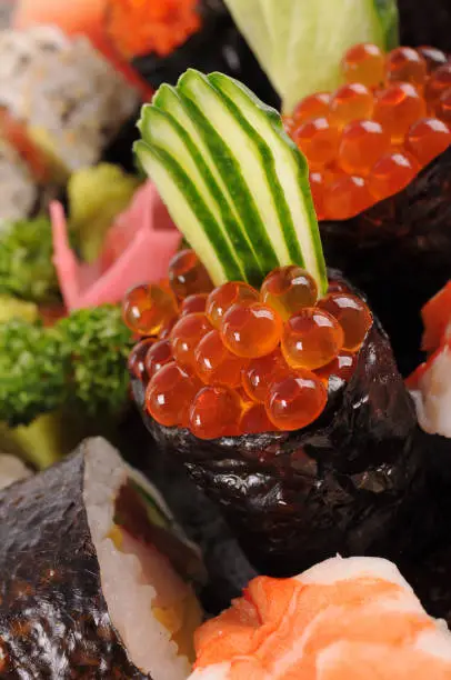 Raw salmon eggs - Ikura sushi with assorted sushi in the background.Here is an alternative version without cucumber garnish: