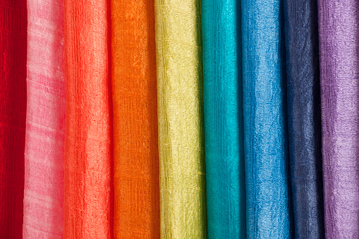 Fragment of rolls of bright colored felt fabric on a white wooden background (Orange, yellow, green, pink)