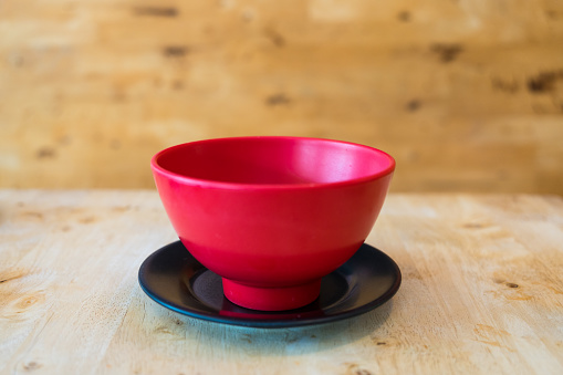 Empty red bowl on a black saucer on wood background. Close up