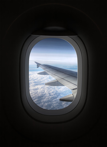 Black airplane window. Outside, you can see an airplane wing and clouds.