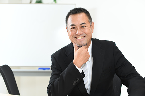 Mature Asian businessman in suit smiling in office