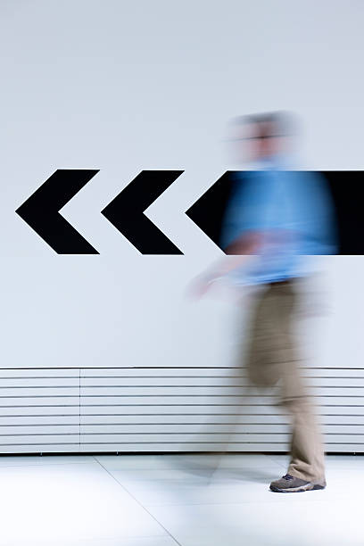 Man walking in opposite direction of arrow a man following an arrow on the wall pointing forward, here you can choose the opposite direction: office leave stock pictures, royalty-free photos & images