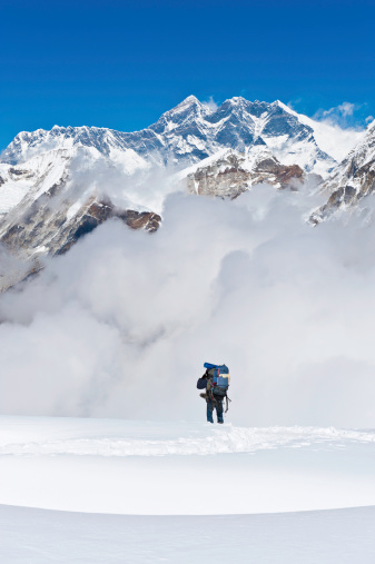 Sherpa mountaineer carrying heavy pack across the snow field glacier of Mera Peak overlooked by the iconic summit pyramid of Mt. Everest, Lhotse and Nuptse deep in the high altitude wilderness of the Nepal Himalaya. ProPhoto RGB profile for maximum color fidelity and gamut.