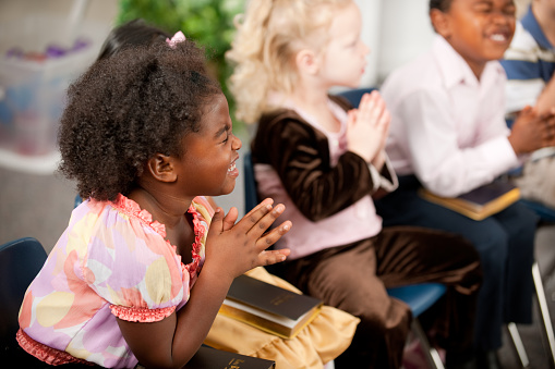 A group of multi-ethnic children at Sunday School in a real church classroom. Very shallow focus. Selective focus on girl closest to the camera 